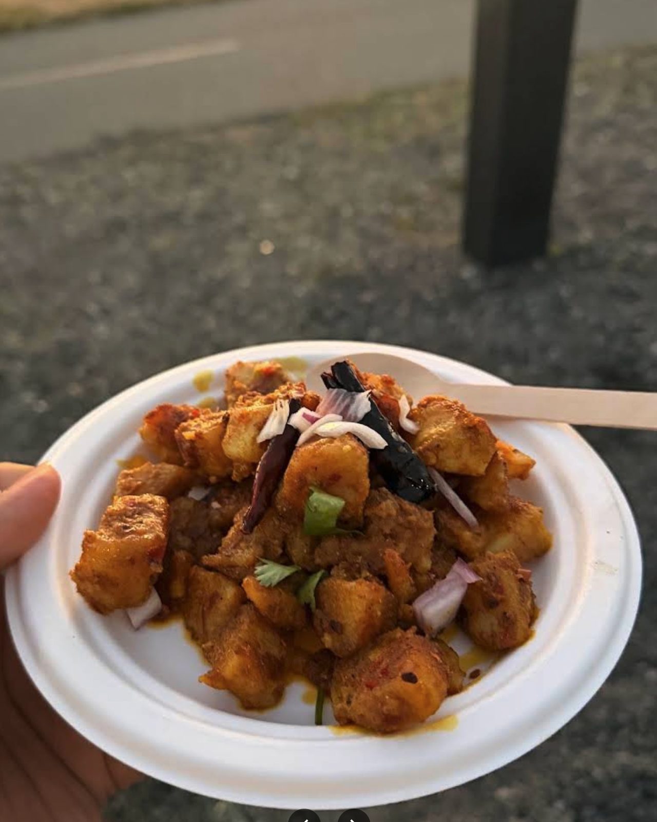 A plate of Amilo Piro potato and choila topped with raw onion, coriander and whole dried chillies
