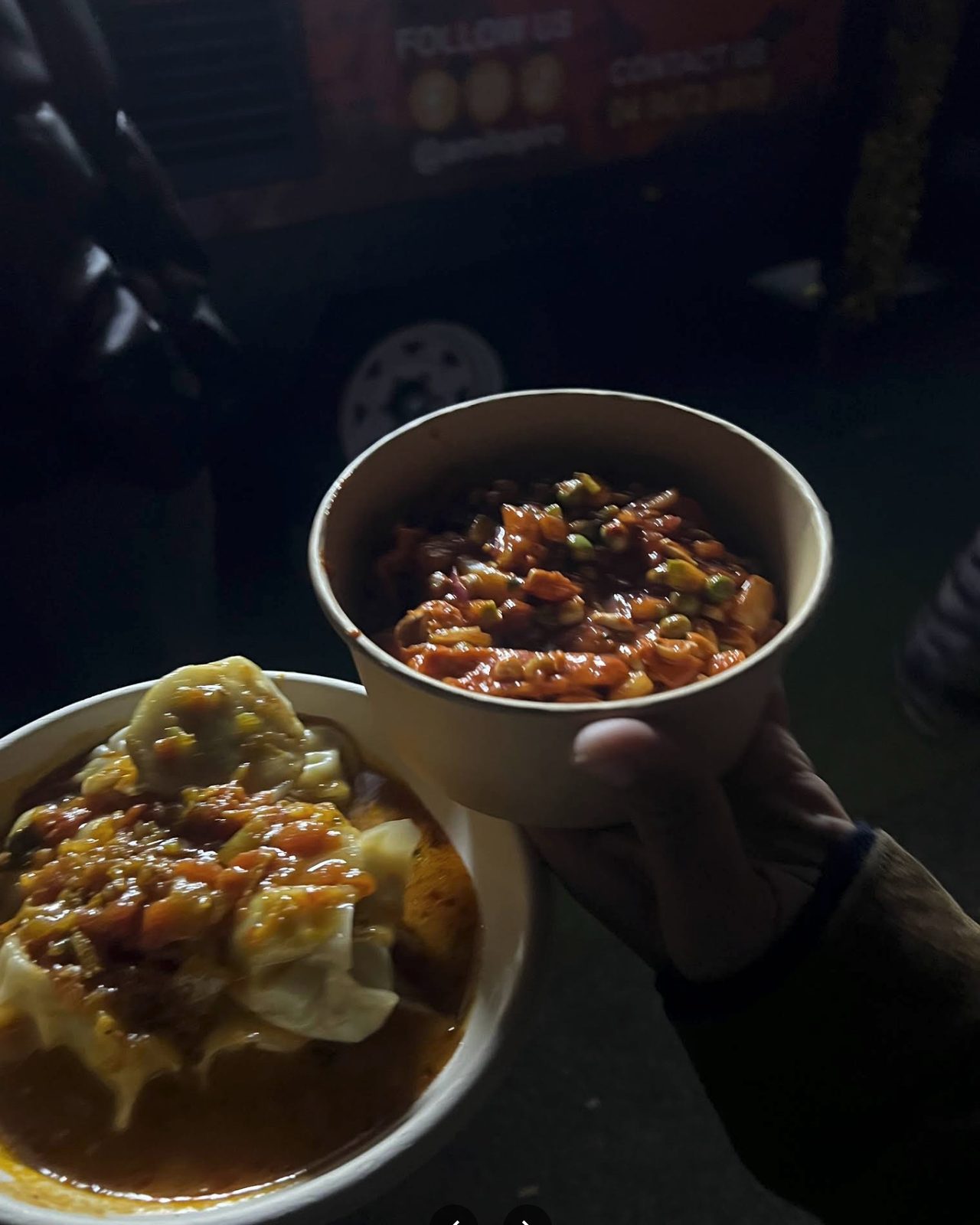A bowl of Amilo Piro jhol momo sitting in its soup beside a cup of chatpate