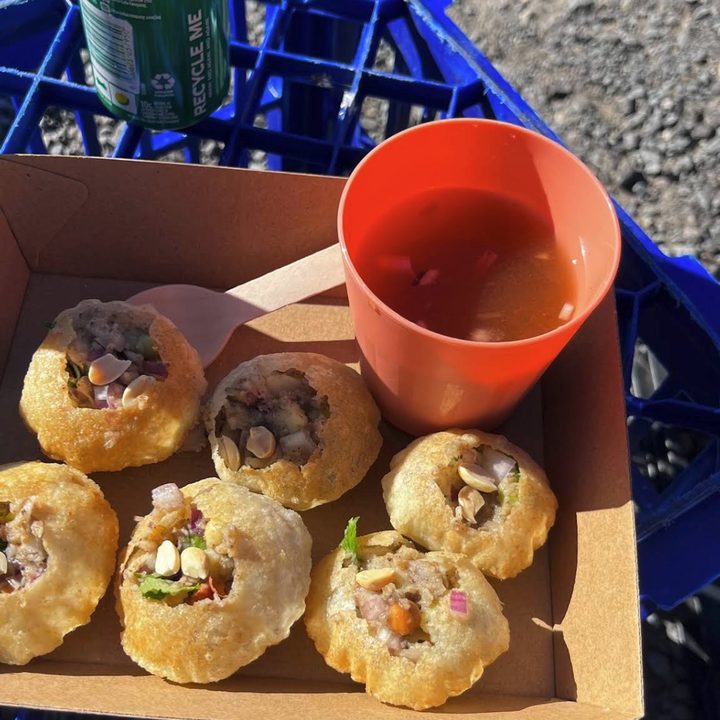 Six Amilo Piro pani puri filled with potato and chickpea, a cup of jhol beside them