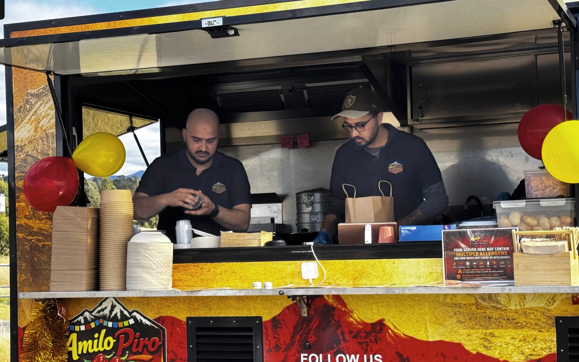 The Amilo Piro van with its serving window open, two staff working inside, the Himalaya artwork and chilli logo across the side panel